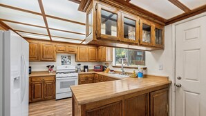 A kitchen with wooden cabinets, a white refrigerator, a stove, and a large island. - Amazing Views! 3,000 sq ft cabin!  Hot Tub, & Game Room! (Big Bear City)