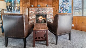 A cozy room with a brick fireplace, leather armchairs, and wooden walls. - Amazing Views! 3,000 sq ft cabin!  Hot Tub, & Game Room! (Big Bear City)