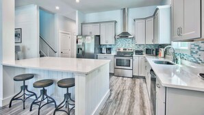 A modern kitchen with white cabinets, a central island with stools, stainless steel appliances, and a tiled backsplash.