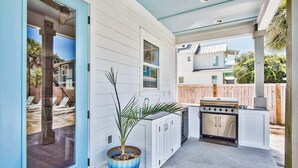 An outdoor kitchen with a grill, cabinets, and a potted plant.