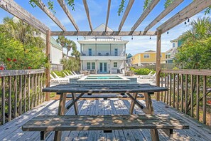 A wooden deck with a pool, surrounded by a wooden pergola and a view of a two-story house with a balcony. - Utopia Estate with Saltwater Pool & Golf Cart (Miramar Beach)