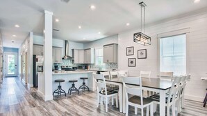 A modern kitchen with white cabinetry, a central island, and a dining area with white chairs and a glass table.
