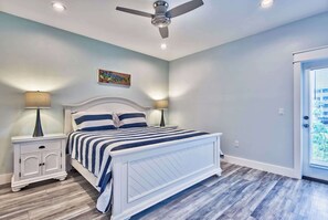 A bedroom with a bed, nightstands, a ceiling fan, and a door with a view. - Utopia Estate with Saltwater Pool & Golf Cart (Miramar Beach)