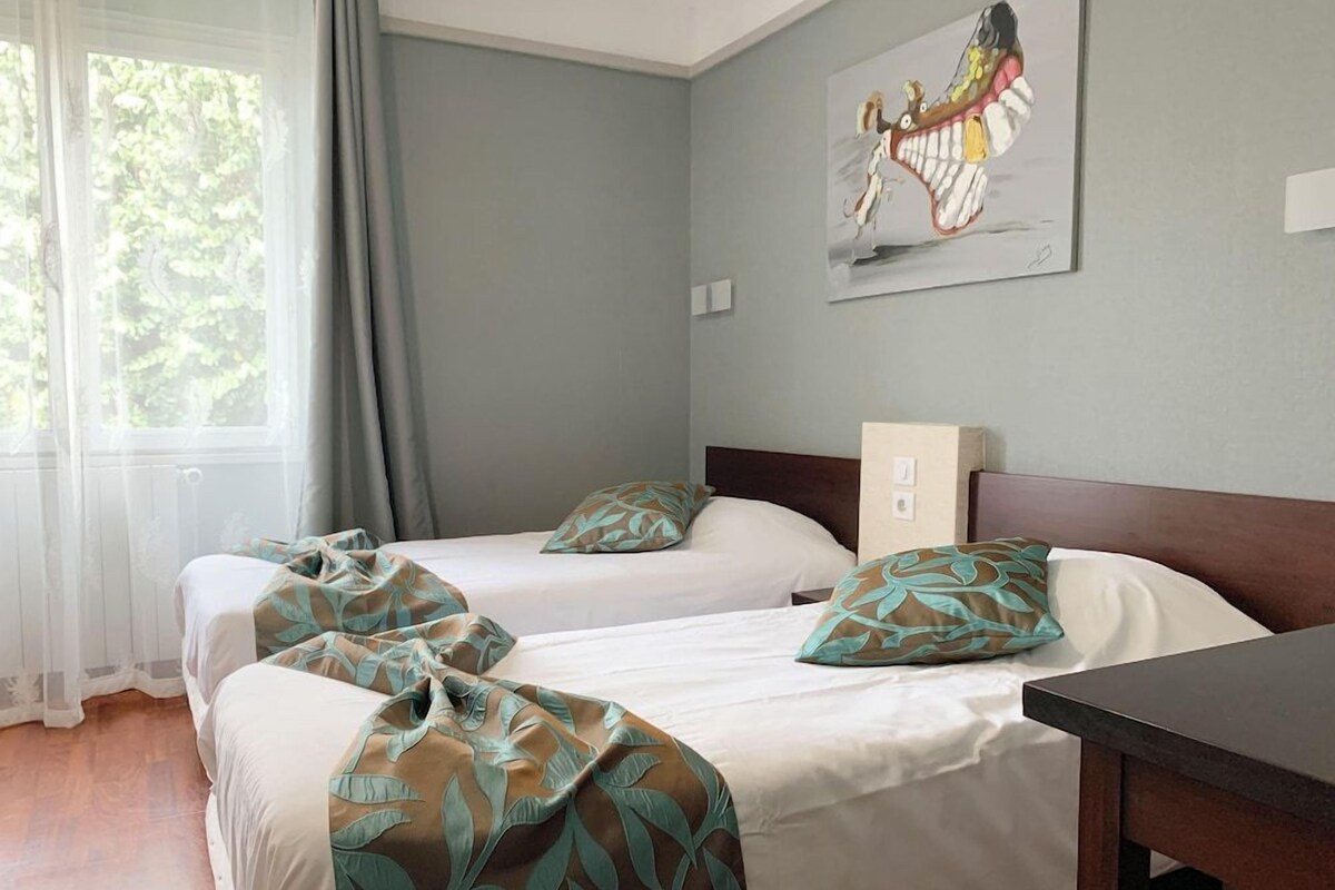 A hotel room with two beds, a table, and a painting on the wall.