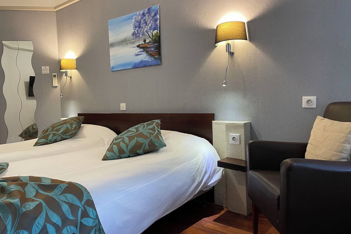 A hotel room with a large bed, two bedside lamps, a painting on the wall, and a chair.