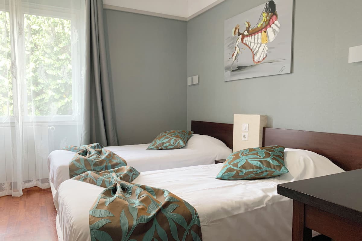 A hotel room with two beds, a wooden headboard, a painting on the wall, and a window with curtains.