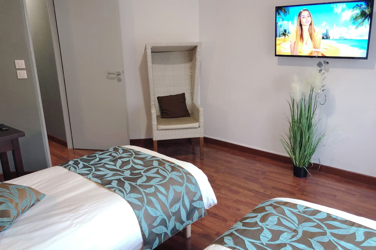 A hotel room with two beds, a television on the wall, a chair, and a plant.
