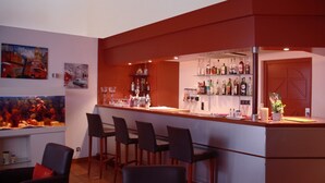 A bar area with a counter, bar stools, and a shelf with bottles. There are paintings on the wall and a fish tank. - L'Embleme Boutique Hotel (Beaurepaire)
