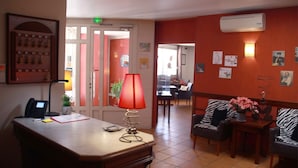 A hotel lobby with a reception desk, a red lamp, a seating area with zebra-patterned chairs, and a wall-mounted air conditioner. - L'Embleme Boutique Hotel (Beaurepaire)