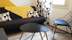 A modern living room with a black sofa, yellow throw, geometric pillows, a black coffee table, and a blue chair. - The Cabanon from the Pas du Loup (la seyne sur mer)