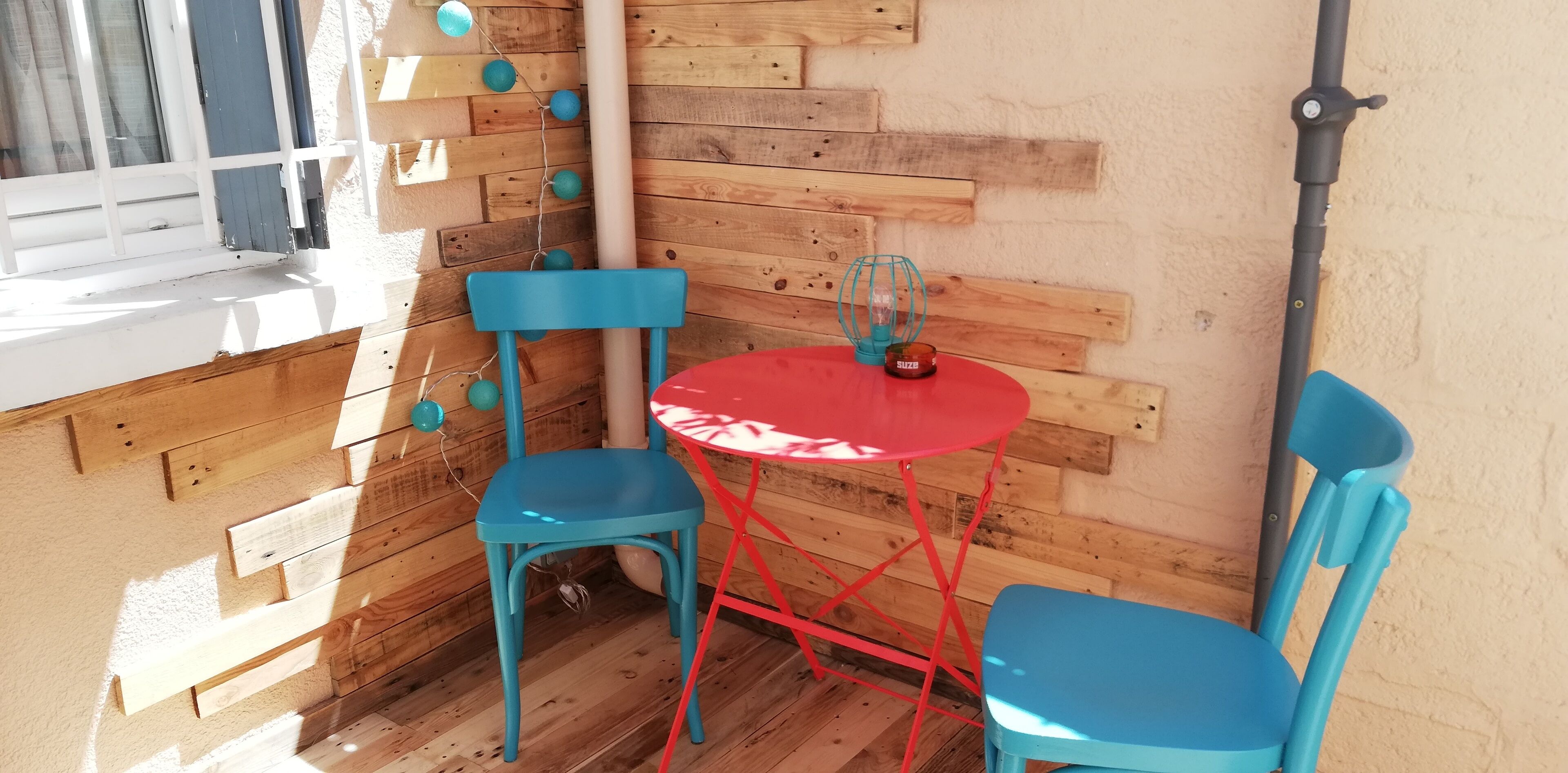 Een hoek met twee blauwe stoelen, een rode tafel en een blauwe lamp.