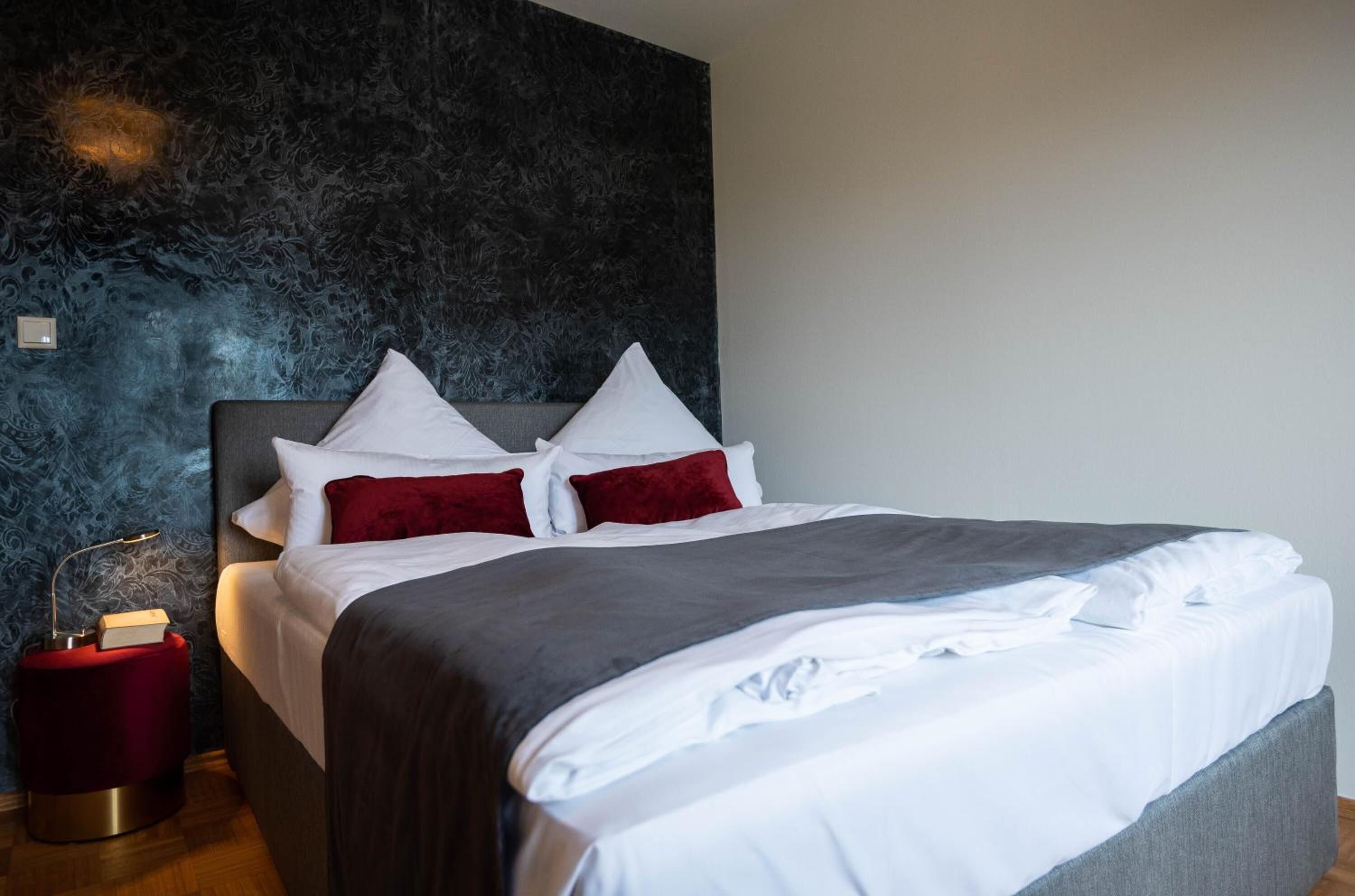A neatly made bed with white and red pillows, a grey blanket, and a dark headboard.