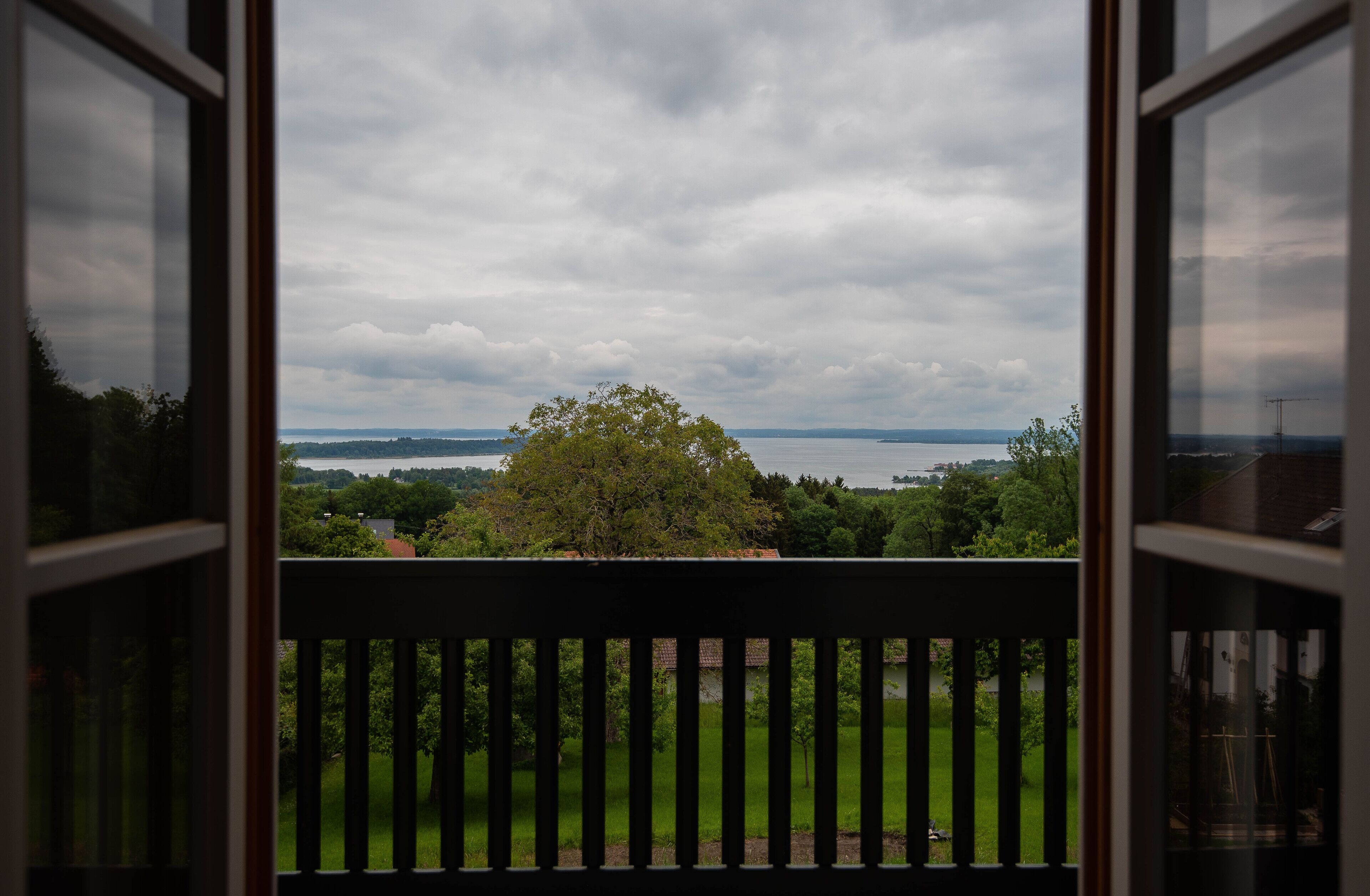 Uitzicht vanaf een balkon met een balustrade, over een gazon en een waterpartij, onder een bewolkte lucht.