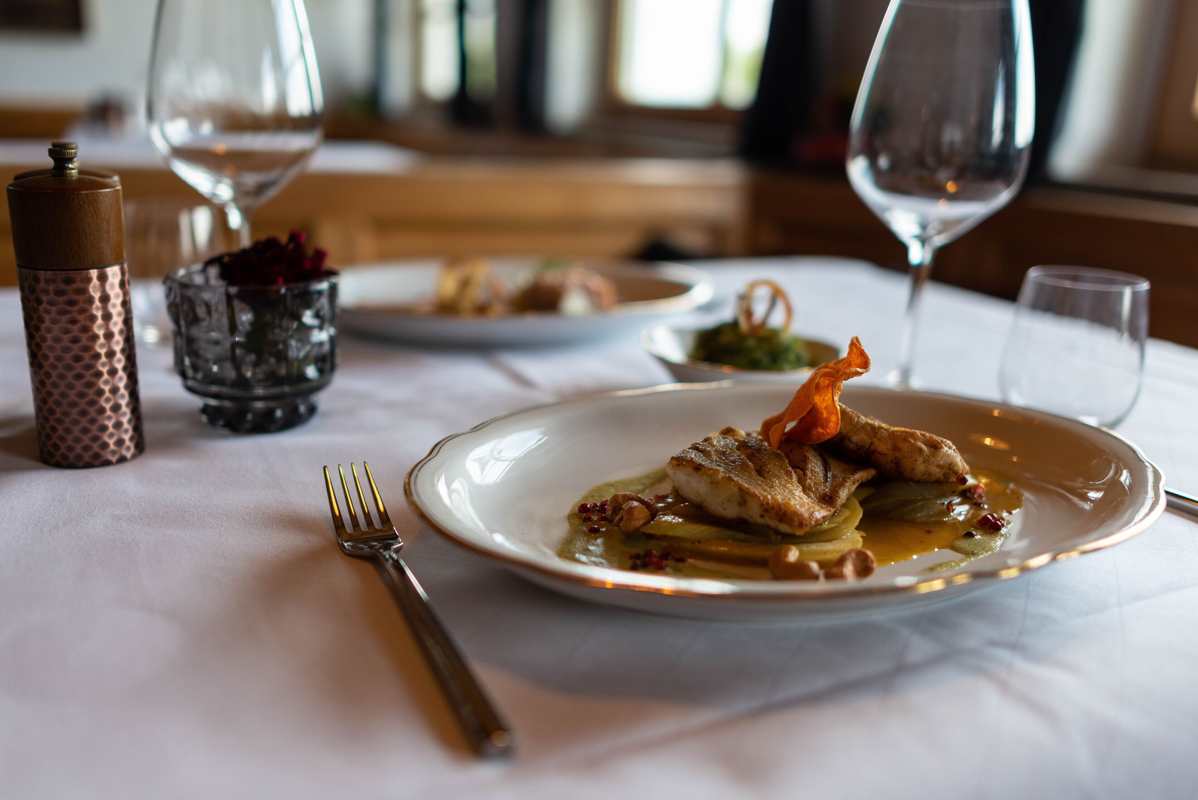 A dining table with plates of food, wine glasses, and cutlery.