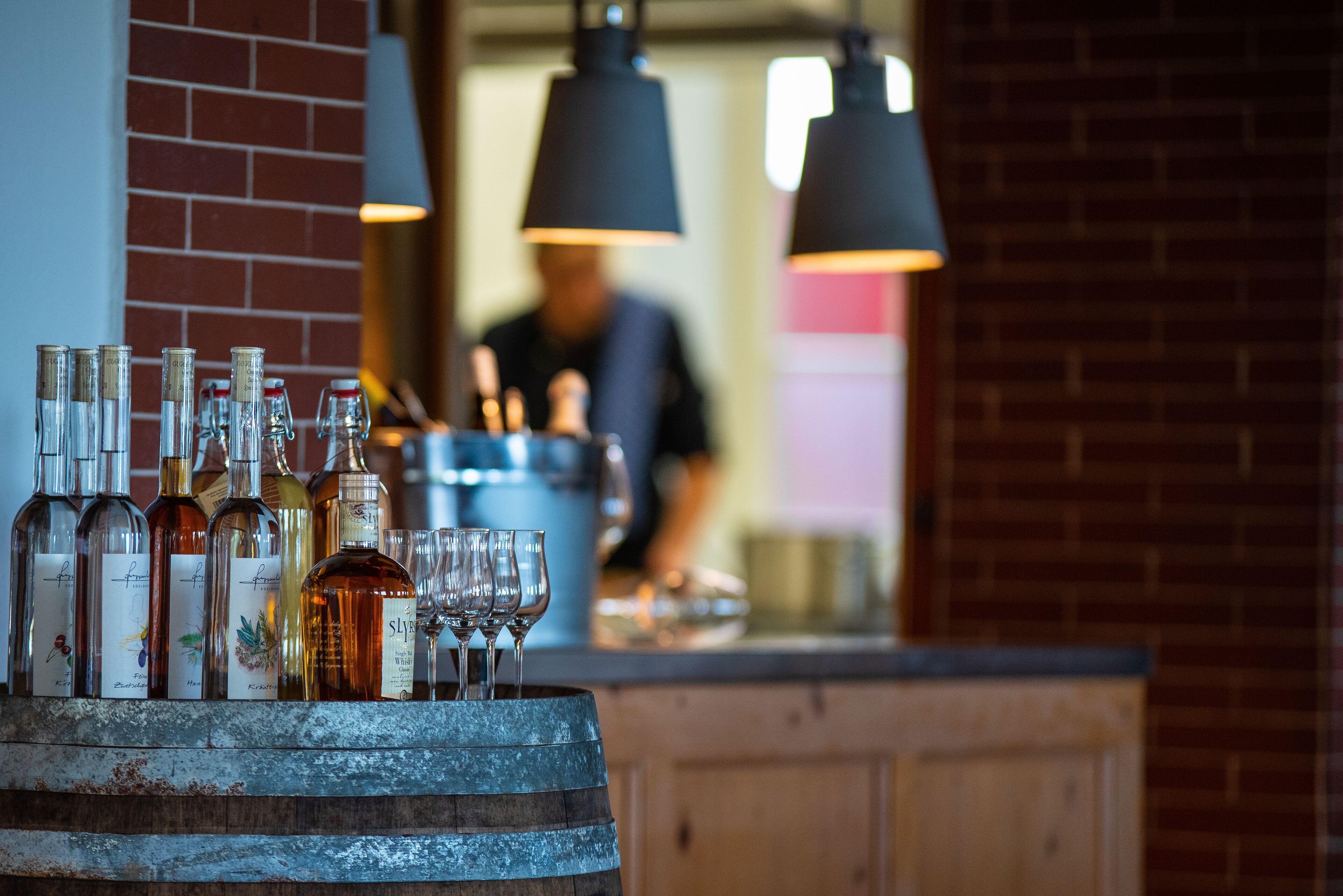 A bar area with a rustic wooden barrel, various bottles, and wine glasses.