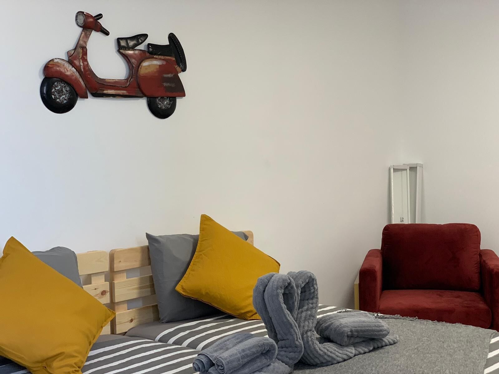 Un dormitorio con una cama, almohadas, una silla roja y un adorno de patinete en la pared.