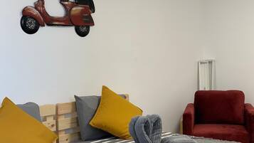 Un dormitorio con una cama, almohadas, una silla roja y un adorno de patinete en la pared.