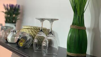 Un jarrón verde con una banda de cuerda sosteniendo flores blancas y tallos parecidos al césped, colocado sobre una superficie oscura junto a tres copas de vino transparentes.