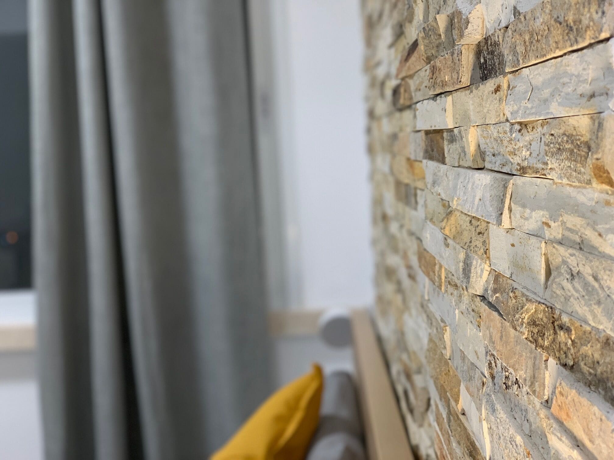 Un muro de piedra con una ventana y cortinas.