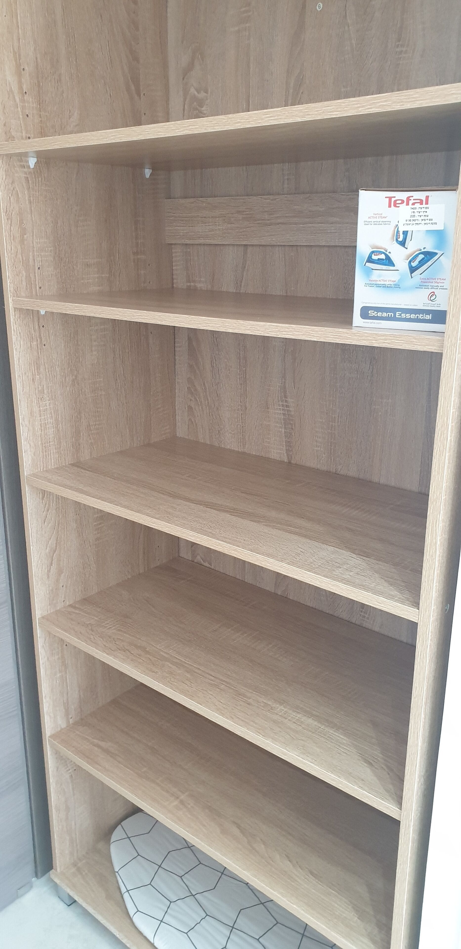 A wooden shelving unit with three shelves and a box labeled "Tefal Steam Essential" on the top shelf.