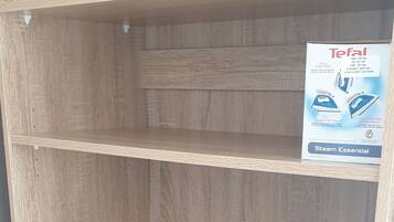 A wooden shelving unit with three shelves and a box labeled "Tefal Steam Essential" on the top shelf.