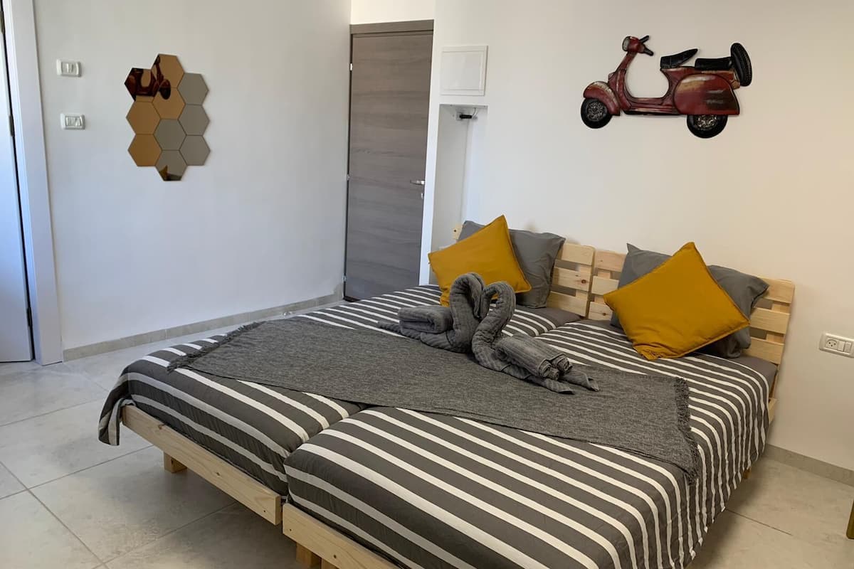 A bedroom with a bed, pillows, a blanket, a wall-mounted scooter decoration, and a hexagonal mirror.