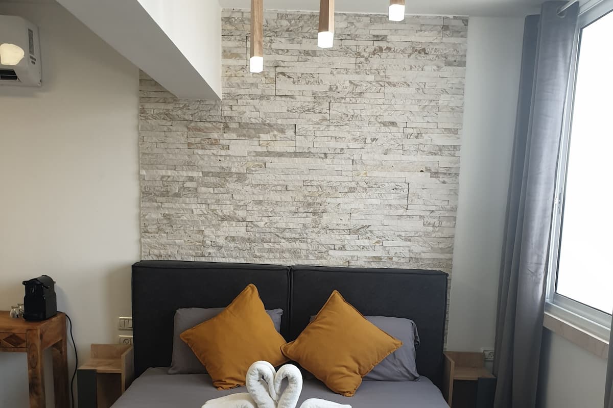 A modern hotel room with a large bed, two brown pillows, a grey blanket, and a unique swan-shaped towel arrangement.