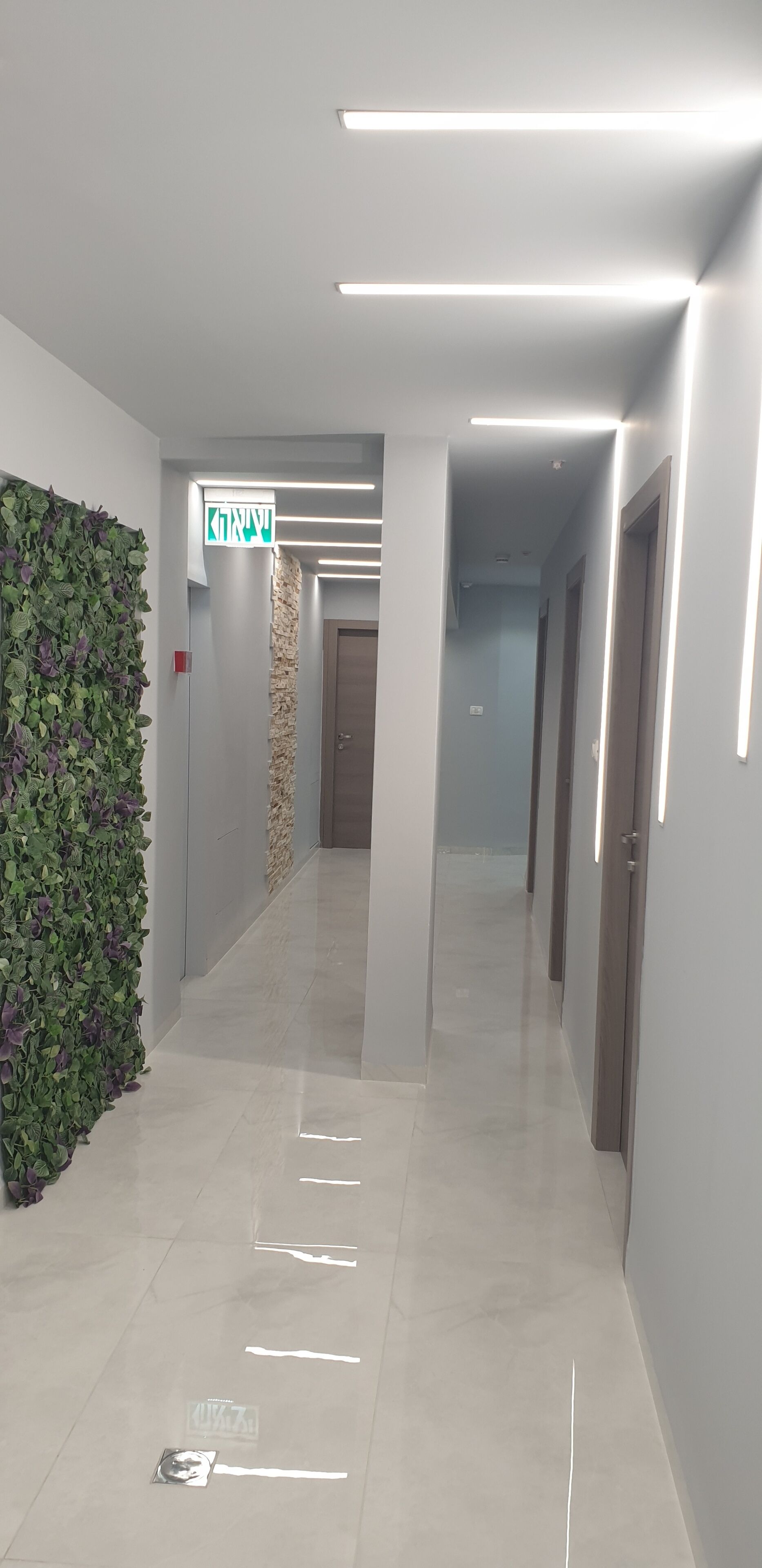 Un pasillo moderno con una pared verde, un muro decorativo de piedra y un cartel que indica una salida.