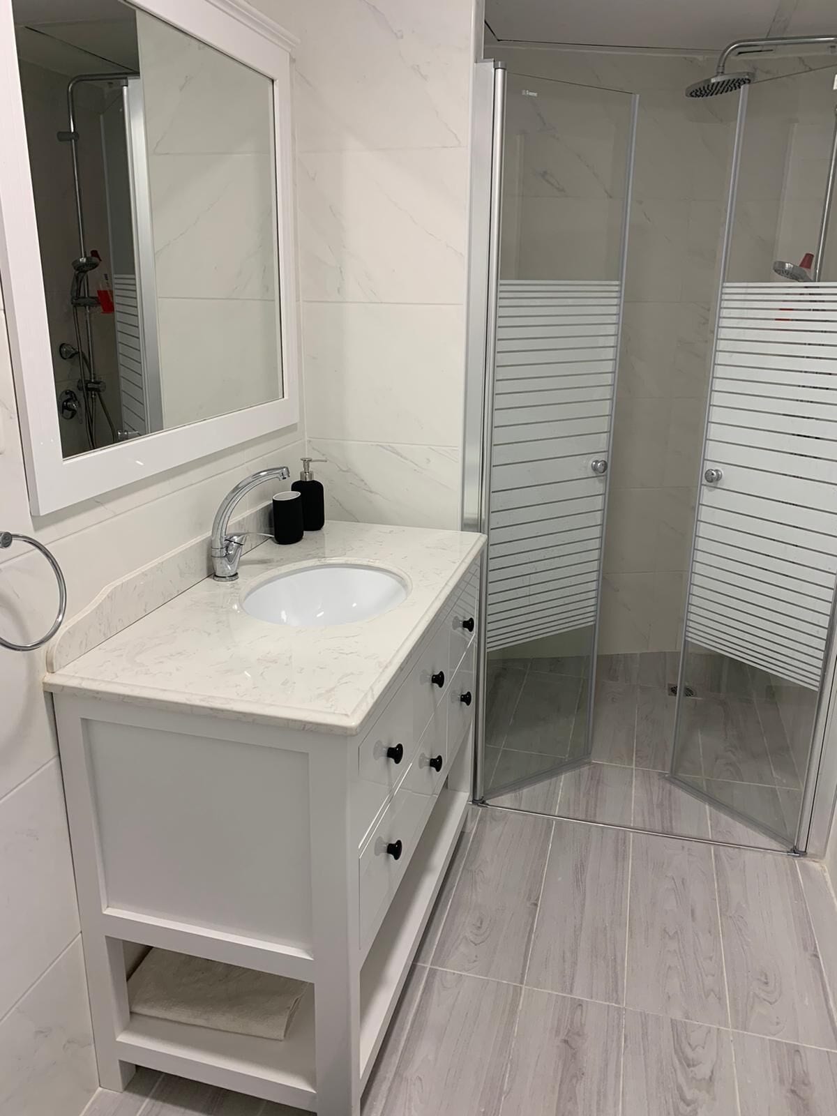 A bathroom with a white vanity, a sink, a mirror, and a glass shower enclosure.