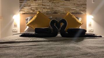 A hotel room with a stone wall, a bed with a dark blanket, two black towels, and two yellow pillows.