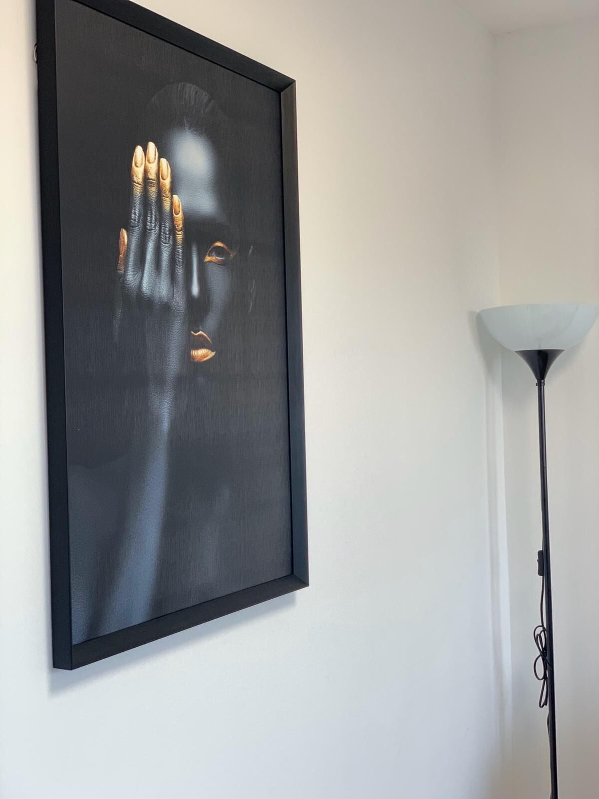 A framed artwork on a wall, a floor lamp to the right, and a white wall.