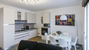 A modern kitchen with white cabinets, a microwave, and a dining area with a glass table and white chairs. - North Milan - Close to metro - Wi-Fi (Milano)