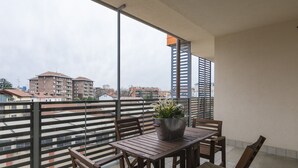 A balcony with a wooden table and chairs, a potted plant, and a view of surrounding buildings. - North Milan - Close to metro - Wi-Fi (Milano)