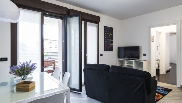 A modern living room with a black sofa, a glass dining table, and a TV on a white stand. - North Milan - Close to metro - Wi-Fi (Milano)