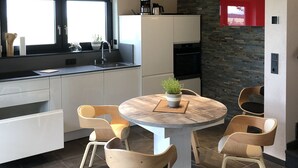 Moderni keittiö, jossa on suuri keittiösaareke, valkoiset kaapit ja kivestä tehty korosteseinä.