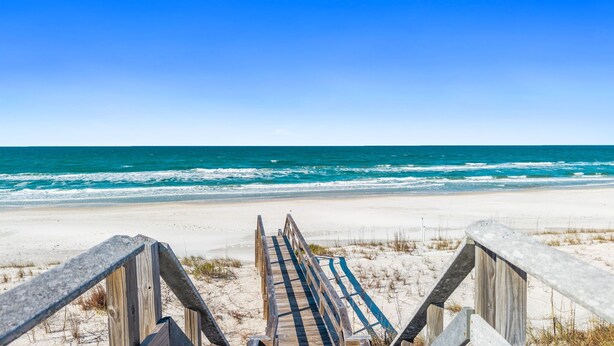 Eine Holztreppe führt zu einem Sandstrand mit Blick auf das Meer.