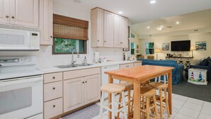 A modern kitchen with white cabinets, a microwave, and a stove. There is a dining area with a wooden table and chairs. - 1 Cassina-Lovely Beach Cottage, Steps to the Sand (Hilton Head Island)