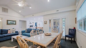 A spacious living area with a dining table, blue sofas, and a ceiling fan. - 1 Cassina-Lovely Beach Cottage, Steps to the Sand (Hilton Head Island)