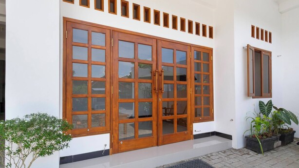 A building with a large wooden door, multiple small windows, and potted plants.