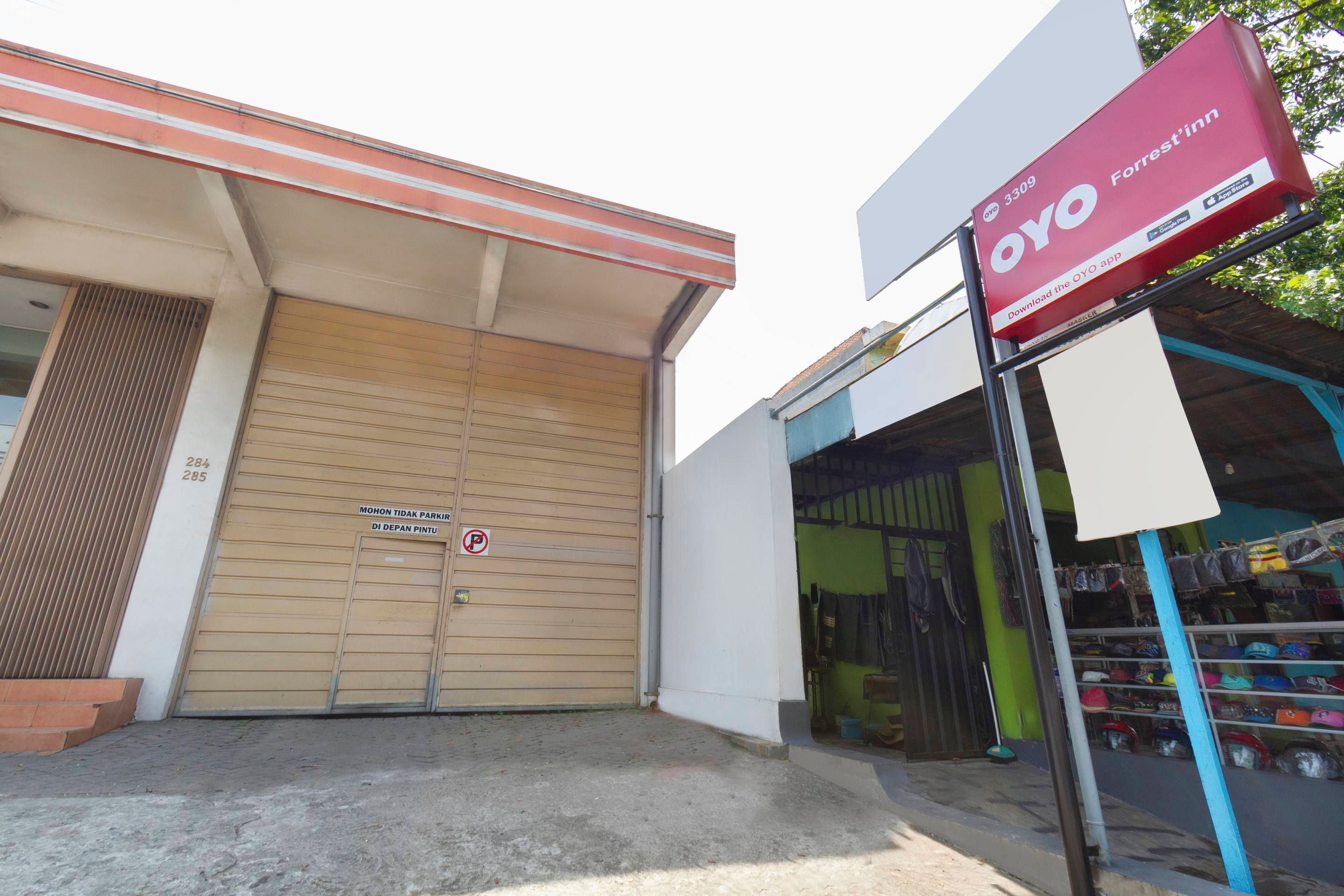 Um edifício com uma porta de obturador fechada, uma placa anunciando OYO Forrest'in e uma vitrine com diversos itens.