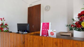 Uma mesa de recepção com computador, relógio e um cartaz.