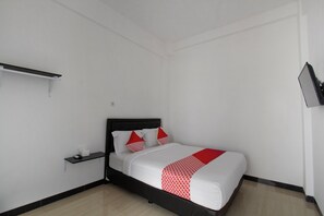 A bedroom with a bed, white walls, a black headboard, a red and white patterned bedspread, and a small shelf with a remote control. - OYO 3309 Forrestinn (Kediri)