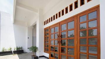 A building with a large wooden door, a tiled patio, and potted plants.