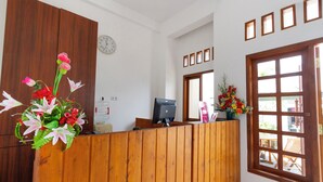 A reception desk with a wooden finish, a clock on the wall, and framed pictures above a window.