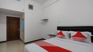 A hotel room with a bed, a wooden door, a small table, and a wall-mounted shelf.