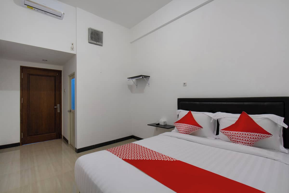Una habitación de hotel con cama, una puerta de madera, una mesita pequeña y un estante en la pared.