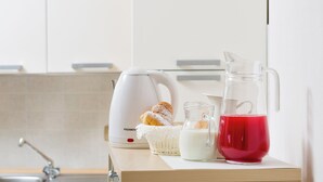 Una encimera de cocina con un hervidor eléctrico blanco, una jarra de vidrio, una cesta con un pastel y un vaso de líquido rojo.