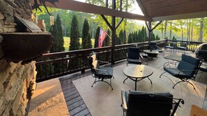 A covered outdoor patio with stone walls, a flag, and outdoor furniture. - Cashiers, NC Home on Golf Course w Trillium Club Access, Fast WiFi, Kid-Friendly (Cashiers)