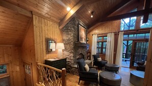 A wooden interior with a stone fireplace, wooden furniture, and large windows. - Cashiers, NC Home on Golf Course w Trillium Club Access, Fast WiFi, Kid-Friendly (Cashiers)