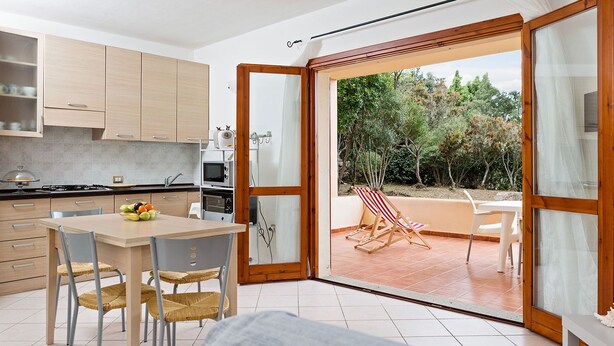Une cuisine moderne avec des meubles en bois, une table à manger avec des chaises, et une vue sur un patio équipé d’une chaise et d’une table.